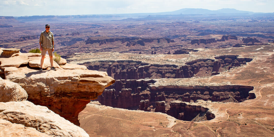man standing on ledge over canyonlands